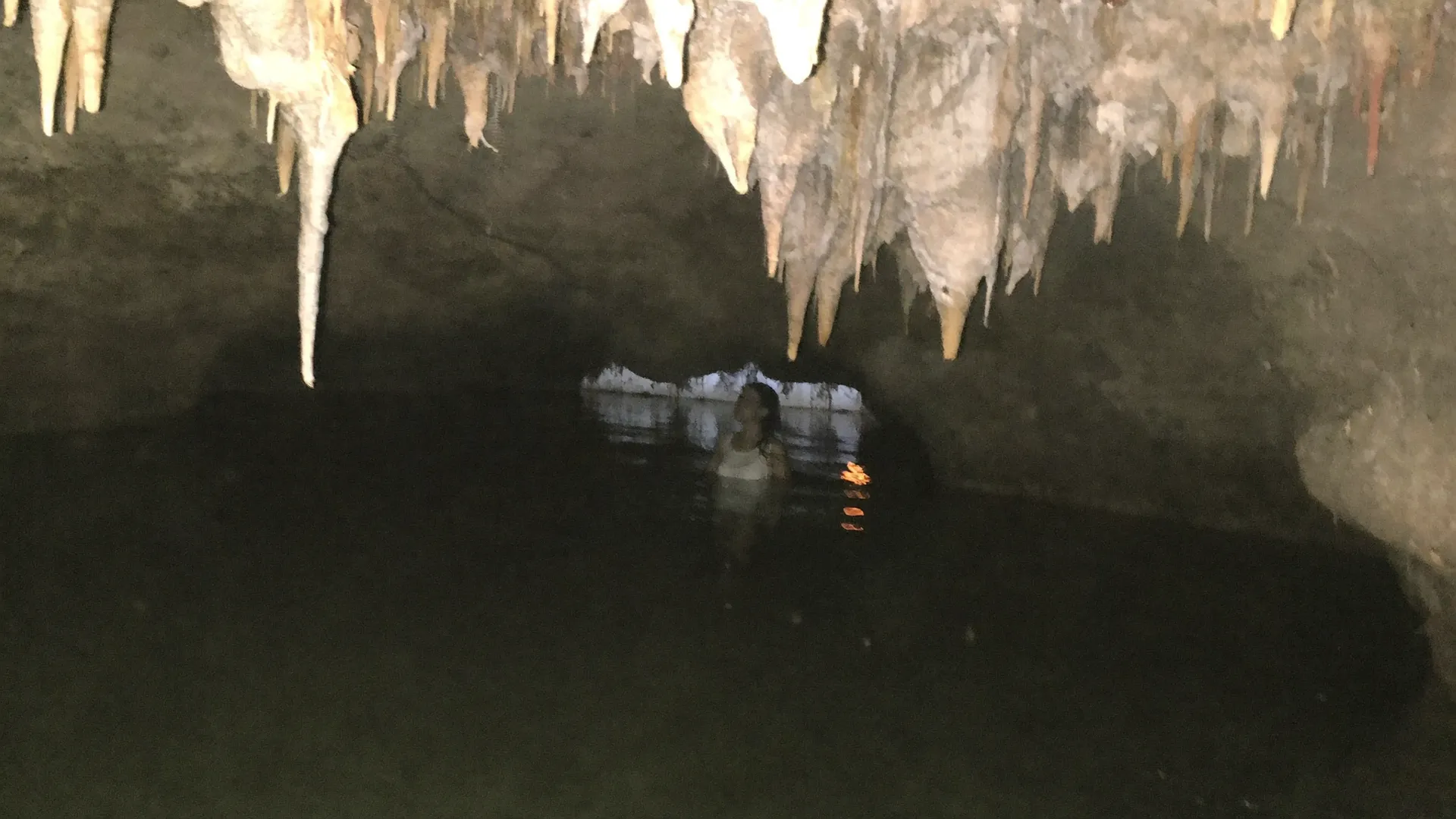 Cenote de caverna con estalactitas y una visitante en el agua cerca de Tulum